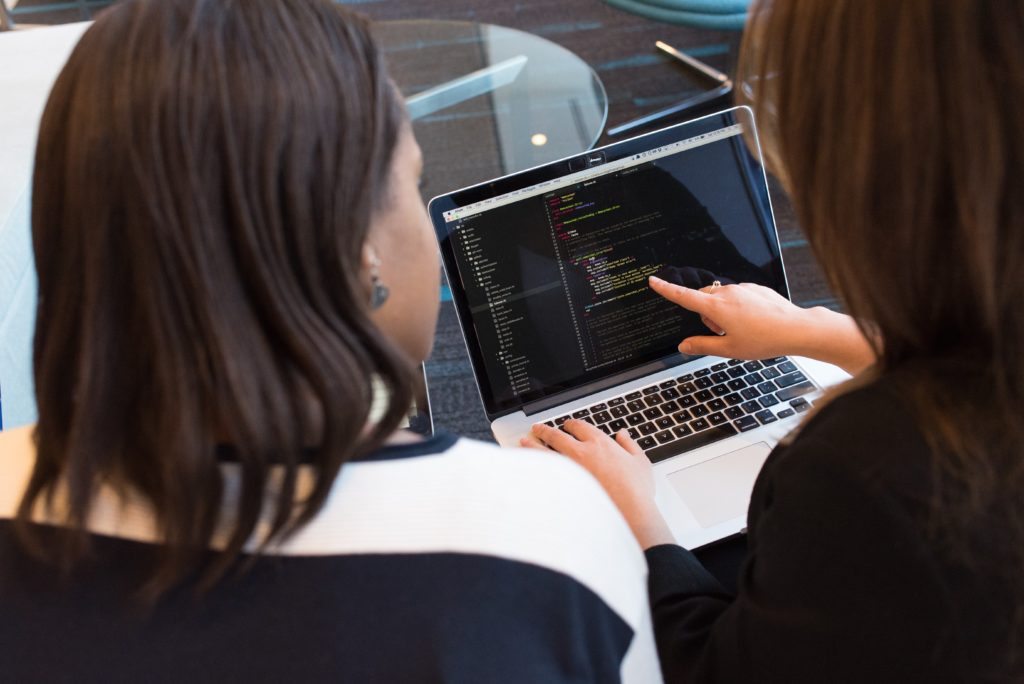 two women looking at code on laptop